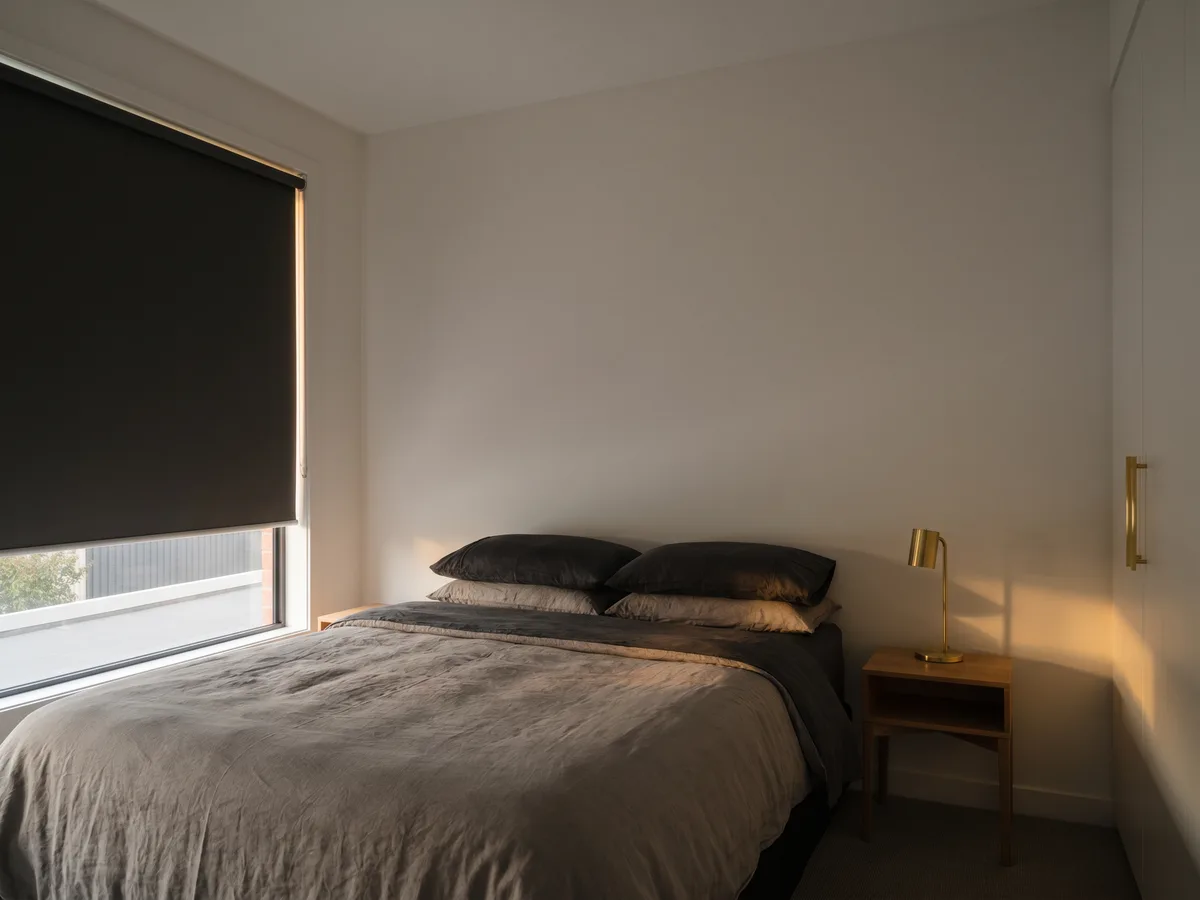 Dim bedroom with a charcoal blockout roller blind fully lowered at first light